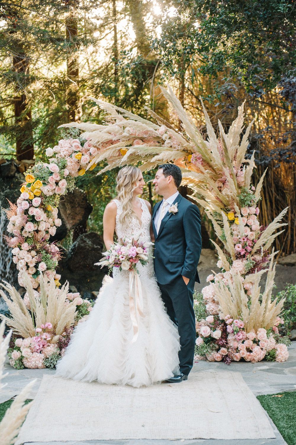 bride and groom smile in front of pampas grass ceremony decor